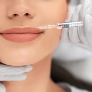 Close up of beautician in white rubber gloves doing injection in lips for young beautiful woman. Concept of process augmentation and improvement lips in professional salon.