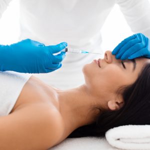 The doctor does injections to correct the hump on the nose with the beauty of young indian woman. The beautician does injections against wrinkles on the face. Women's cosmetology in a beauty salon.
